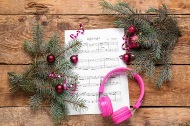 Müzik kağıtları, modern kulaklıklar ve ahşap arka planda Noel süslemeleri olan kompozisyon