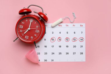 Adet takvimi, alarm saati ve pembe arka planda kadın hijyen ürünleri.