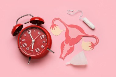 Kağıt rahim, kadın hijyen ürünleri ve pembe arka planda çalar saat kompozisyonu