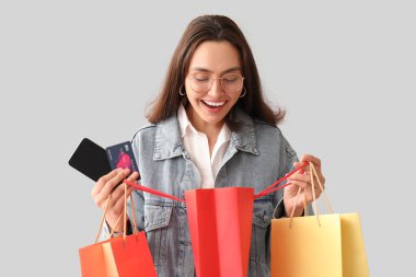 Kredi kartı, cep telefonu ve beyaz arka planda alışveriş torbaları olan genç bir kadın.