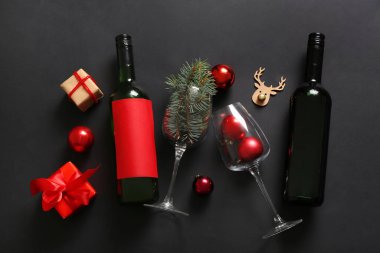 Gözlüklü şarap şişeleri hediye kutuları ve siyah arka planda Noel süslemeleri.