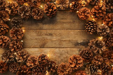 Çam kozalaklarından yapılmış bir çerçeve Noel ışıkları ahşap arka planda parlıyor