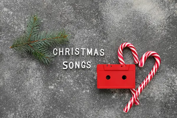 Composition with text CHRISTMAS SONG, audio cassette and candy canes on grunge background
