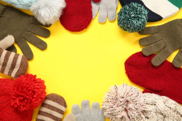 Frame made of different warm gloves, mittens and hats on yellow background