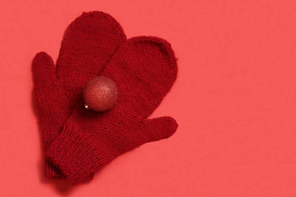 Warm mittens and Christmas ball on red background