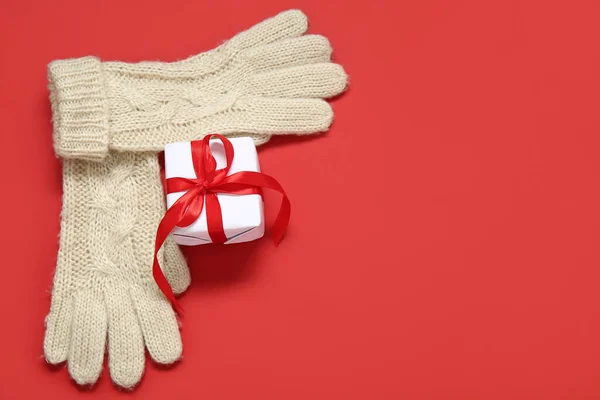 Warm gloves and Christmas gift on red background