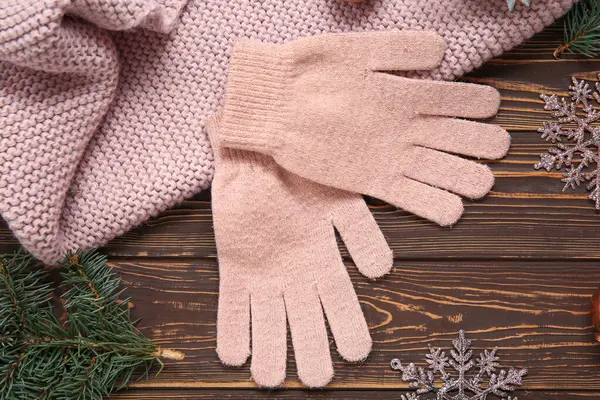 Warm gloves, scarf and Christmas decorations on wooden background