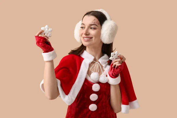 美しい若い女性はベージュの背景に装飾的な雪片でサンタクロースとして服を着ています — ストック写真