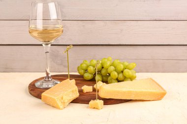 Lezzetli parmesan peynirli ahşap tahta, masada bir bardak şarap ve üzüm.