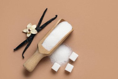 Kahverengi arka planda aromatik vanilya şekeri, çiçek ve sopalarla ahşap kepçe.