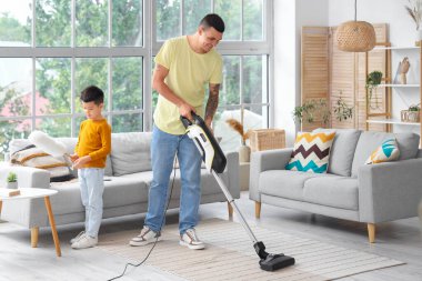 Genç bir adam ve küçük oğlu evde halı süpürüyor.