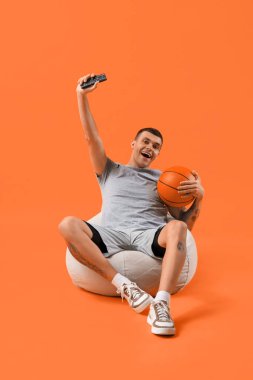 Turuncu arka planda top izleyen genç adam.