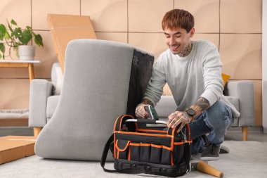 Elinde bir çanta alet olan genç adam evinde sandalye monte ediyor.