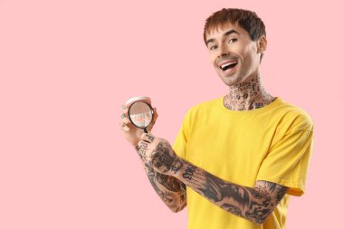 Genç dövmeli adam pembe arka planda çene modelini büyütüyor