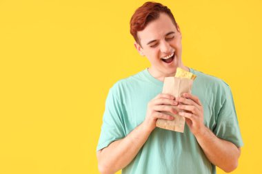 Sarı arka planda lezzetli sandviçli genç adam.