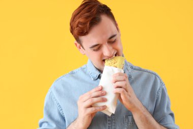 Sarı arka planda lezzetli sandviçler yiyen genç adam, yakın plan.