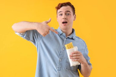 Genç adam sarı arka plandaki lezzetli sandviçi işaret ediyor.