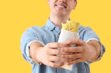 Sarı arka planda lezzetli sandviçli genç adam, yakın plan.