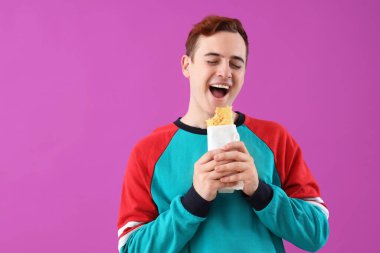 Genç adam mor arka planda lezzetli sandviçler yiyor.