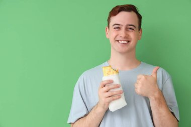 Lezzetli sandviçli genç adam yeşil arka planda baş parmağını kaldırıyor.