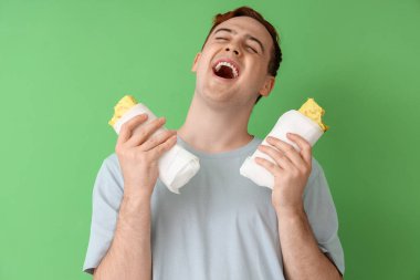 Yeşil arka planda lezzetli sandviçleri olan mutlu genç adam, yakın plan.