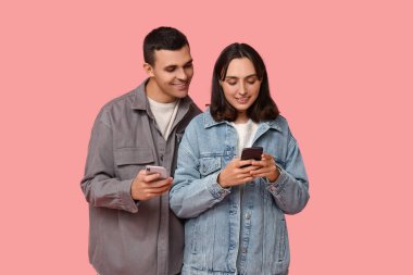 Pembe arka planda cep telefonları olan mutlu genç çift.