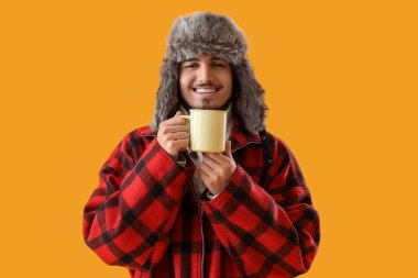 Sarı arka planda bir fincan sıcak çay ve kışlık elbiseli genç adam.