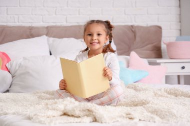 Yatak odasında kitap okuyan tatlı küçük kız.