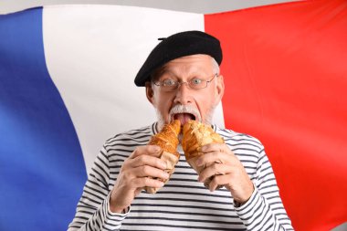 Kıdemli adam Fransa bayrağına karşı lezzetli kruvasanlar yiyor.