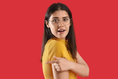 Genç dedikoducu kadın kırmızı arka plandaki bir şeyi işaret ediyor.