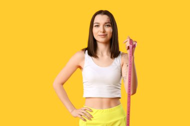 Beautiful young sporty woman with measuring tape on yellow background. Weight loss concept clipart