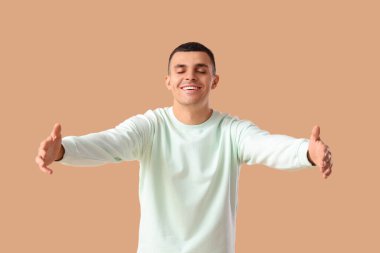 Genç adam bej arka planda sarılmak için kollarını açıyor.