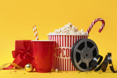 İçkili bir kova patlamış mısır, film makarası ve sarı arka planda Noel hediyesi.