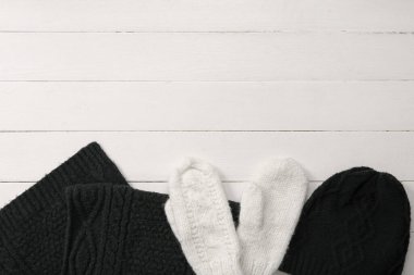 Beyaz ahşap arka planda, kalın şapkalı ve atkılı bir çift eldiven.