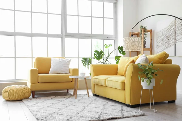 Interior of light living room with yellow sofa and armchair near big window