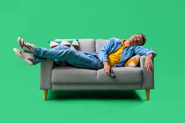 Junger Mann Mit Fernbedienung Schläft Auf Sofa Vor Grünem Hintergrund — Stockfoto