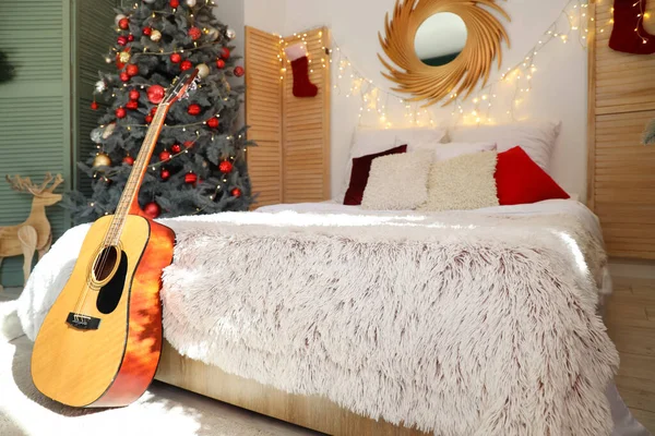 Cozy Christmas bedroom interior with decorated fir tree and guitar