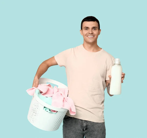 Young man with laundry basket and bottle of detergent on blue background