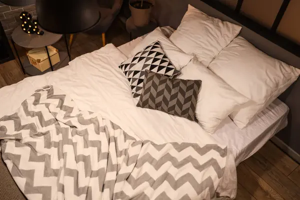 Bed with pillows and blanket in bedroom at night, top view
