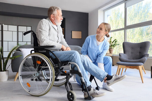 Senior man in wheelchair with nurse at home