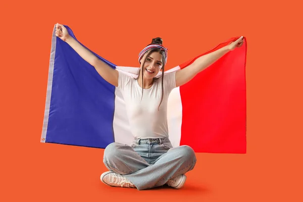 Young woman with flag of France sitting on orange background