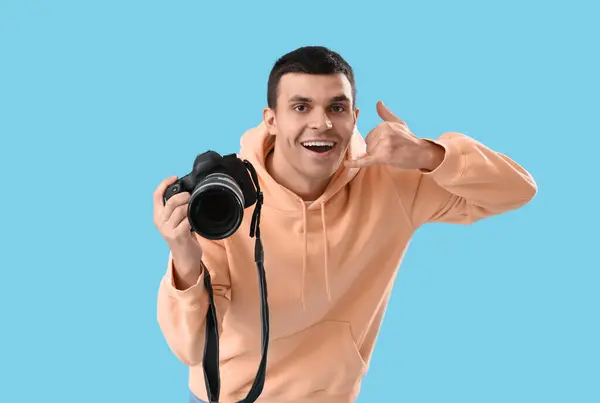 青い背景に 私を呼ぶ ジェスチャーを示すカメラを持つ男性写真家 — ストック写真