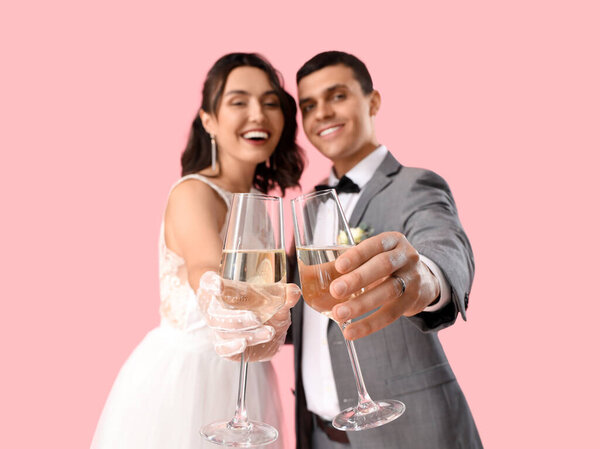 Молодая супружеская пара с бокалами шампанского на розовом фоне