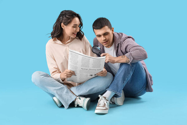 Young couple with newspaper and magnifier on blue background