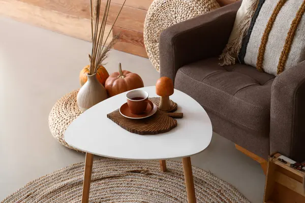 Stylish interior of living room with autumn decor and cup of tea on table