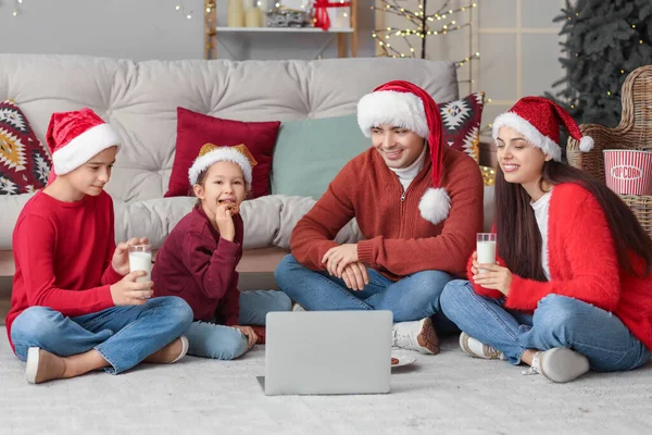 Happy family with milk and cookies watching Christmas movie on laptop at home