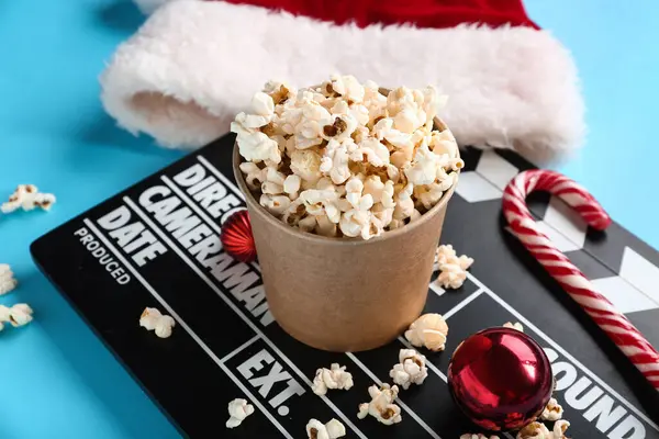 Bucket of popcorn with movie clapper and Christmas decor on blue background