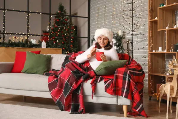 Genç bir kadın Noel arifesinde sıcak kakao içiyor.