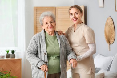 Genç bakıcı yatak odasındaki yaşlı kadına yardım ediyor.