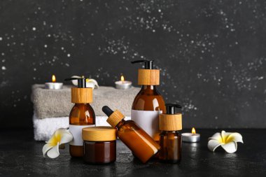 Farklı kozmetik ürünleri, temiz havlular ve koyu arkaplanda yanan mumlar içeren kompozisyon